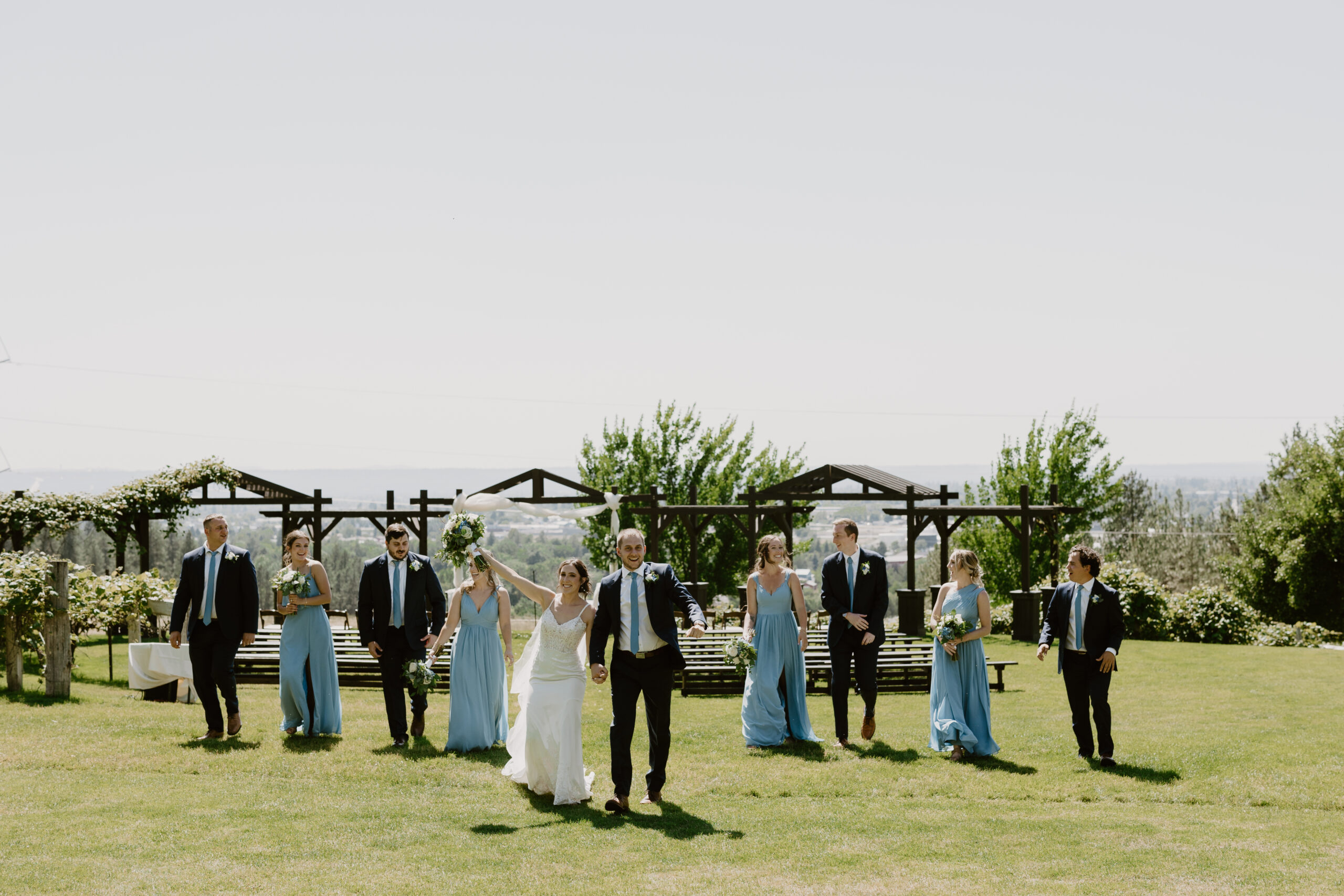 a bride and groom with their bridal party walking across a field of grass at beacon hill in spokane washington