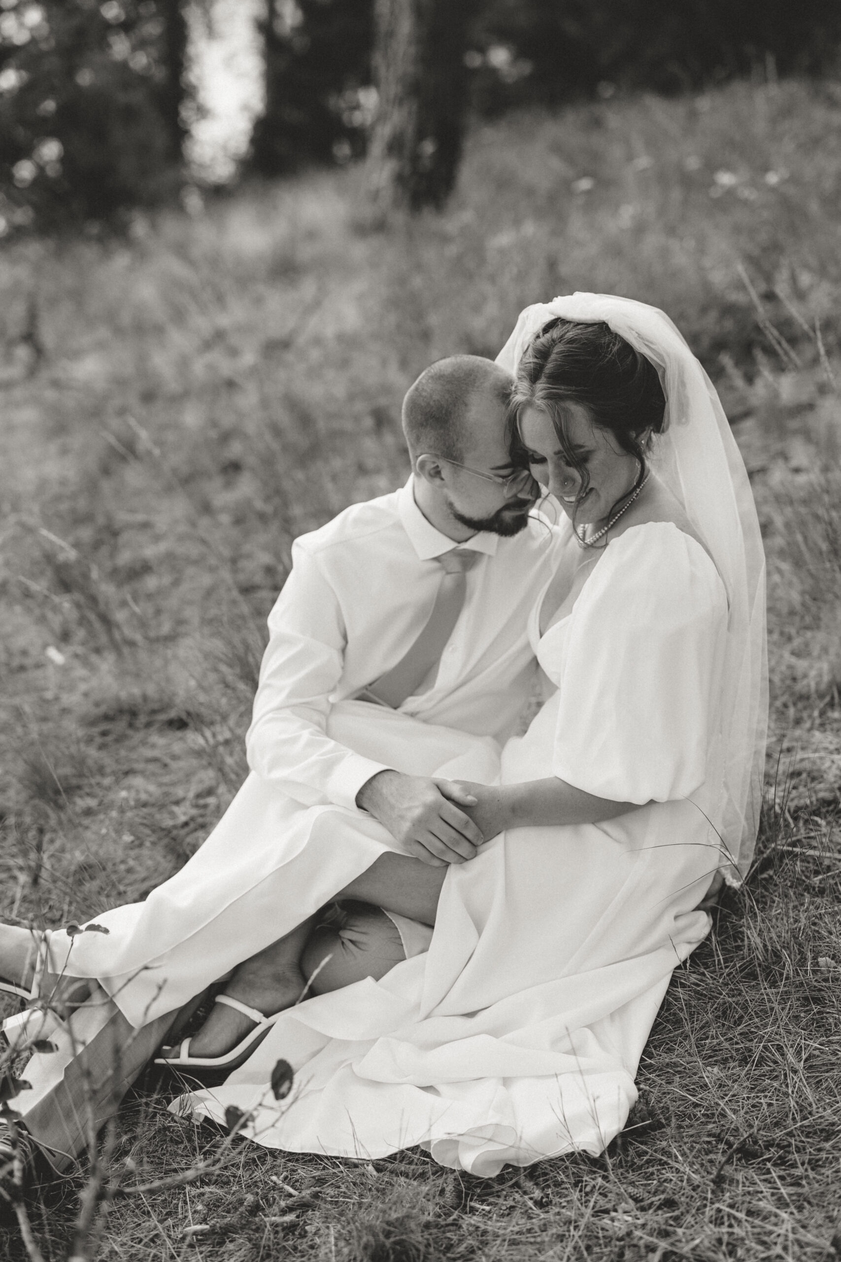 a bride and groom sitting on the floor of a forrest holding hands with their foreheads pressed togeher