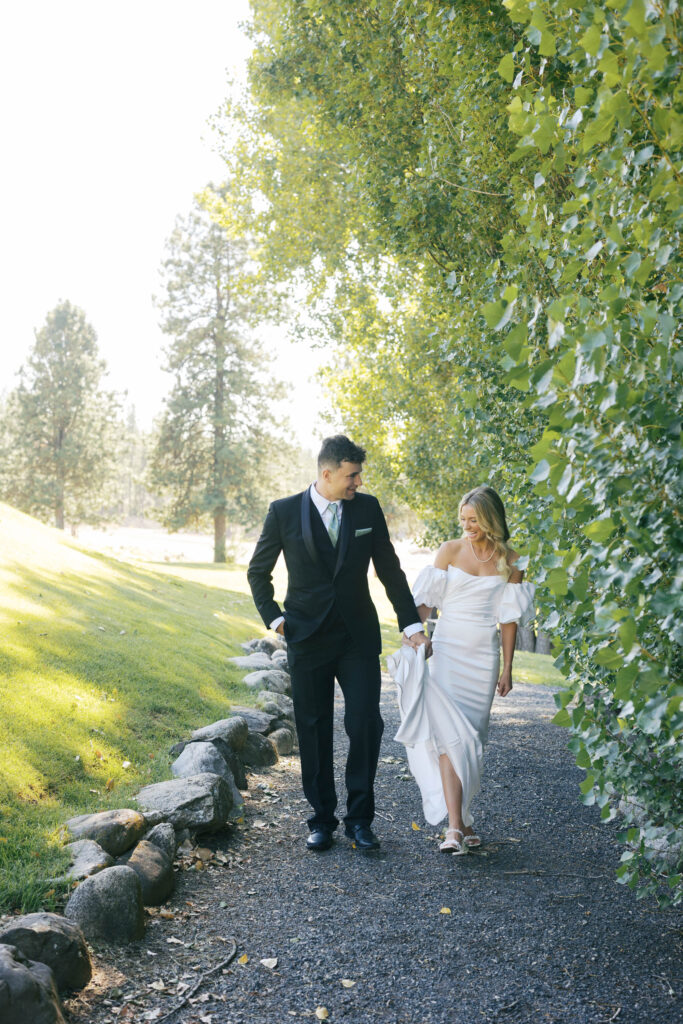 bride and groom walking towards the camera laughing, groom is holding the brides dress. 