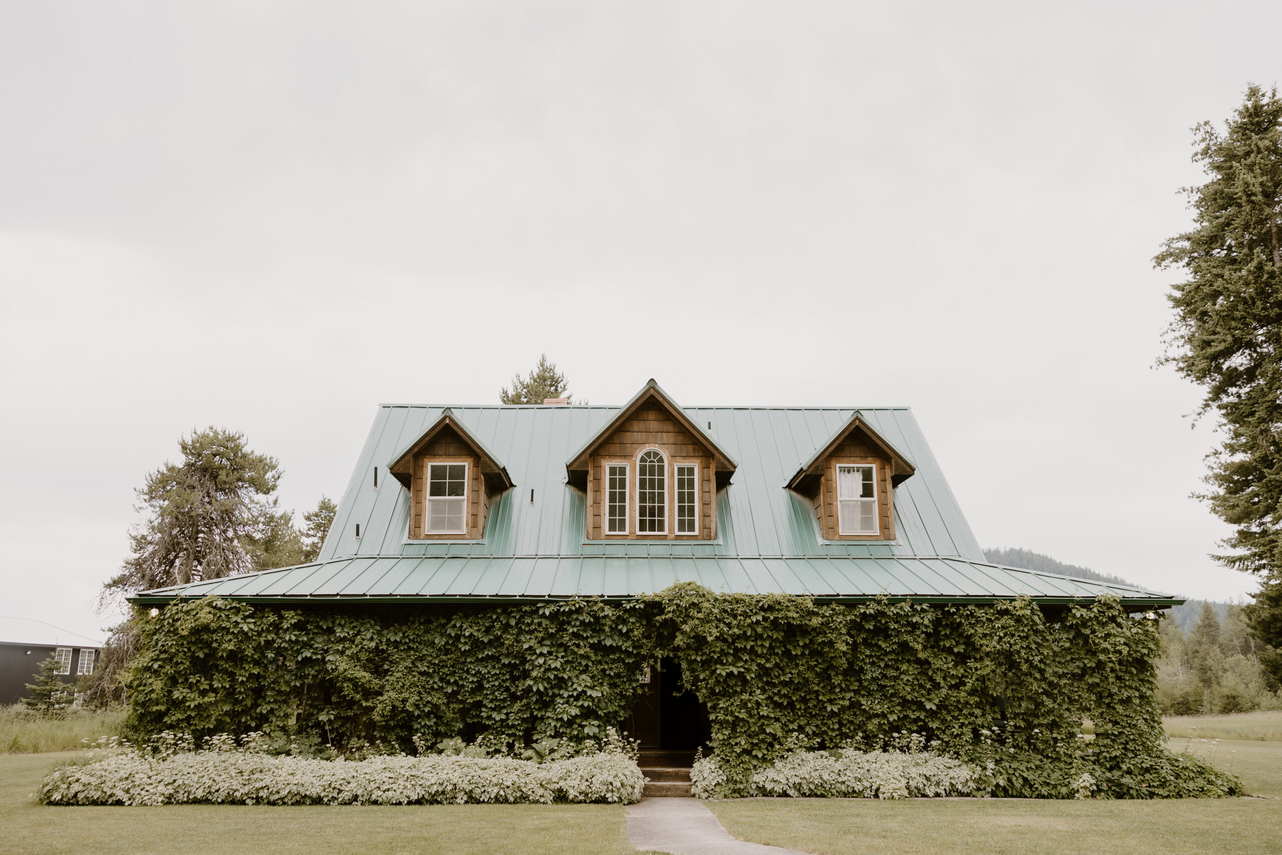 Exterior view of The Wild Rabbit wedding venue near Spokane, WA, covered in ivy with mountain backdrop, photographed by Spokane wedding photographer Arch and Elm Photography