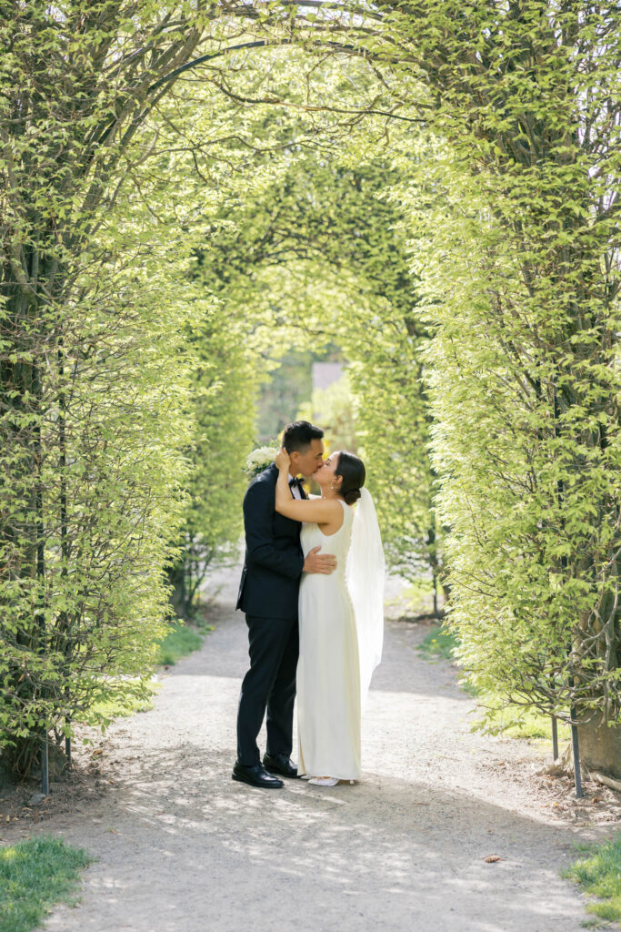 Bride and groom kiss under arched greenery path in Manito Park