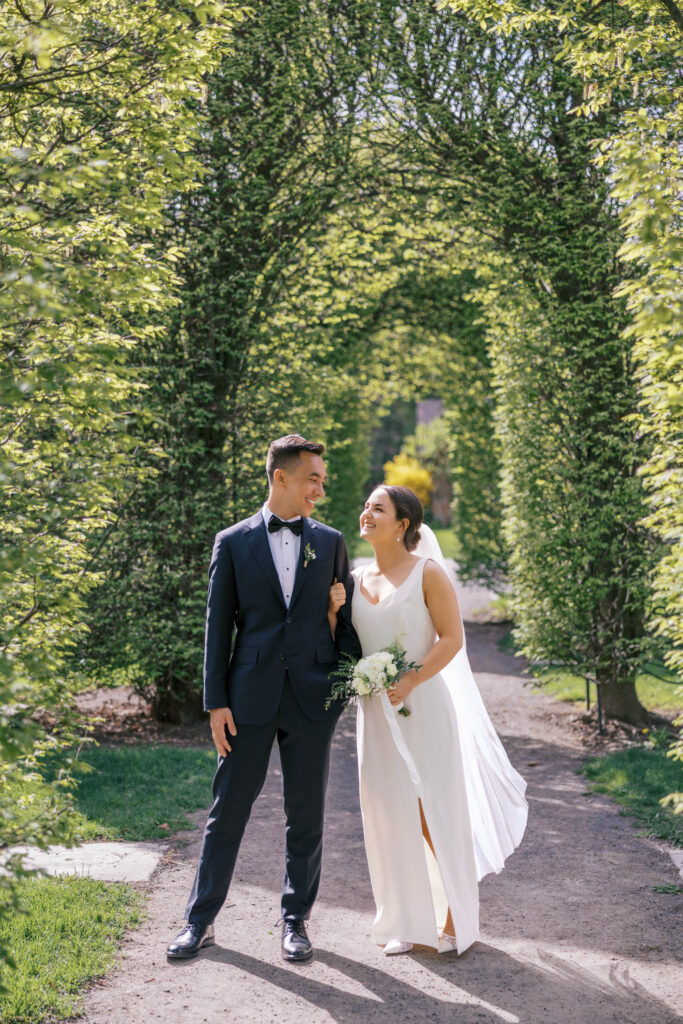 Bride and groom smiling at each other under green garden arch at Manito Park