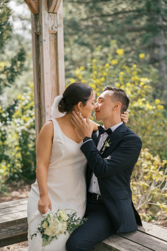 A bride is sitting on the grooms lap and they are about to kiss in Manito Park. 