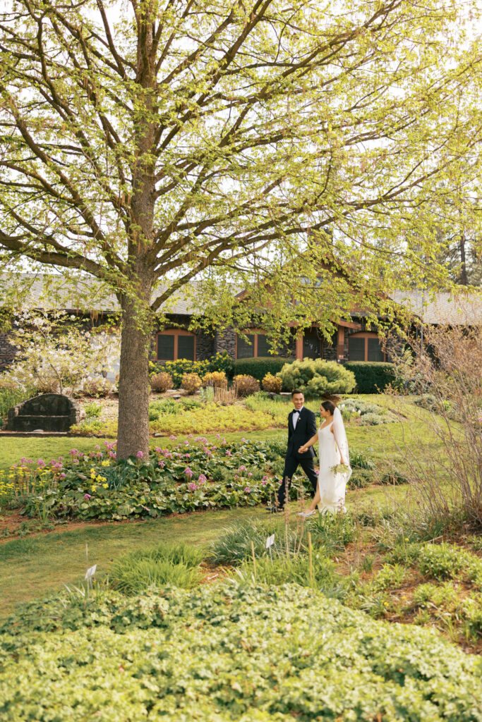 A bride and groom are holding hands and smiling at each other as they walk through the perennial garden at Manito Park.