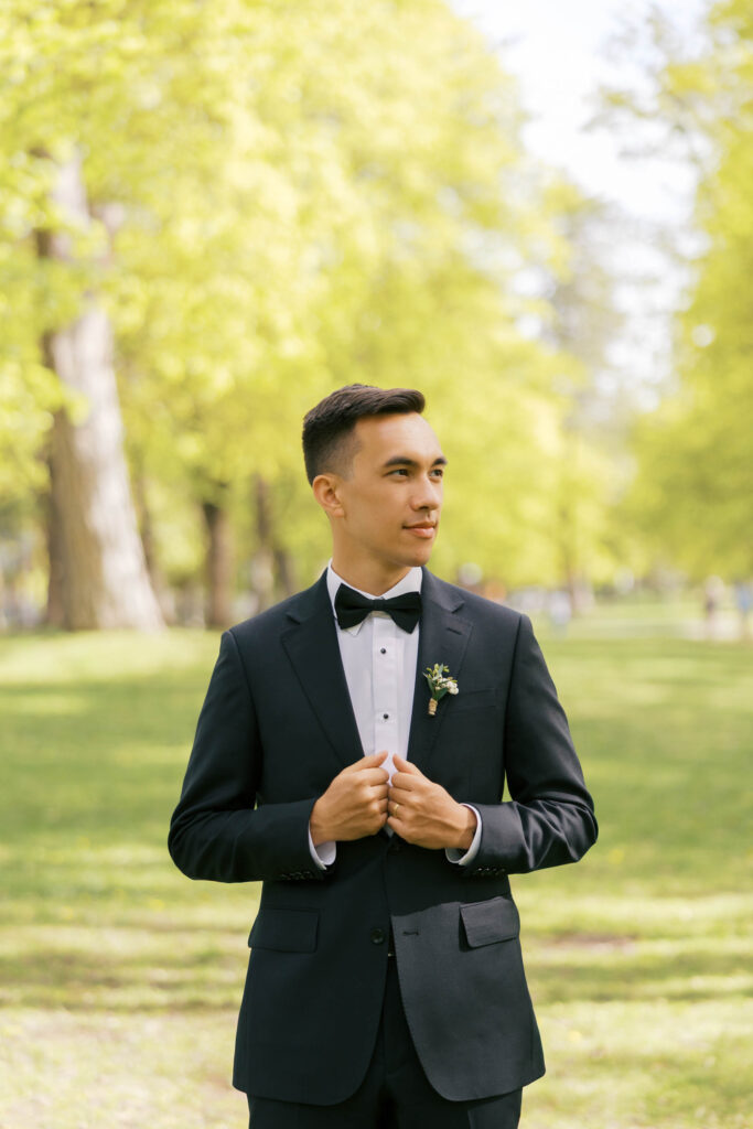 A groom holding the chest part of his suit while looking off to the side. 