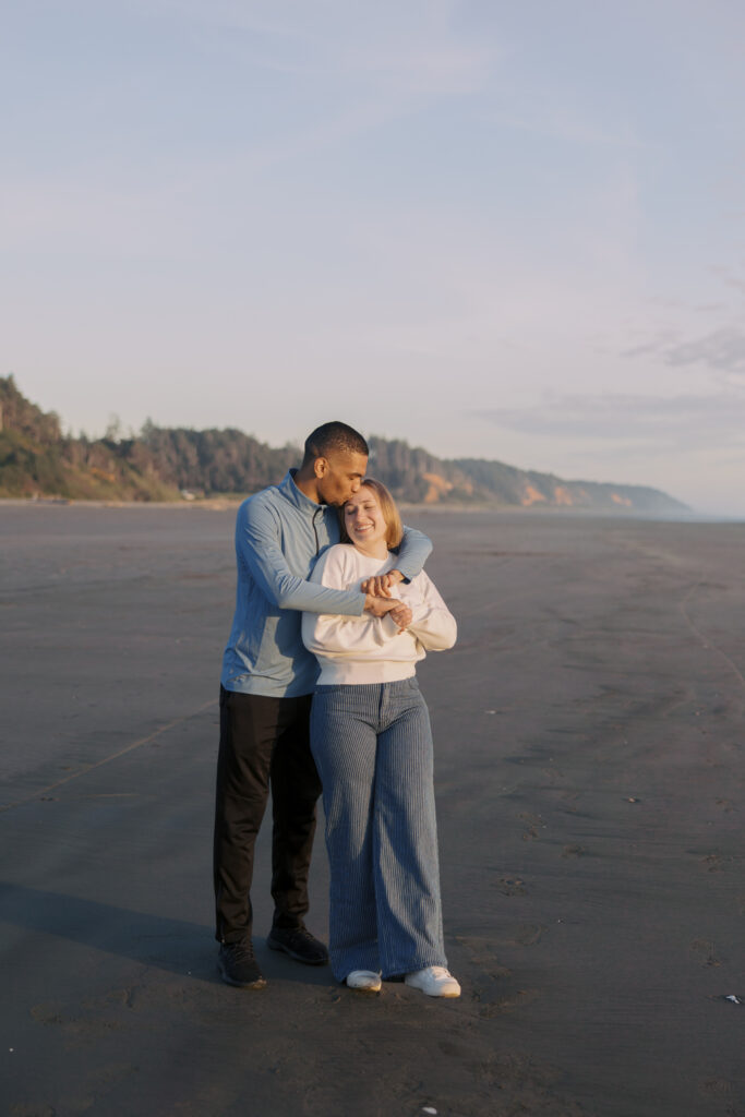 A'lon kissing the top of Julia's head as they stand together on the beach