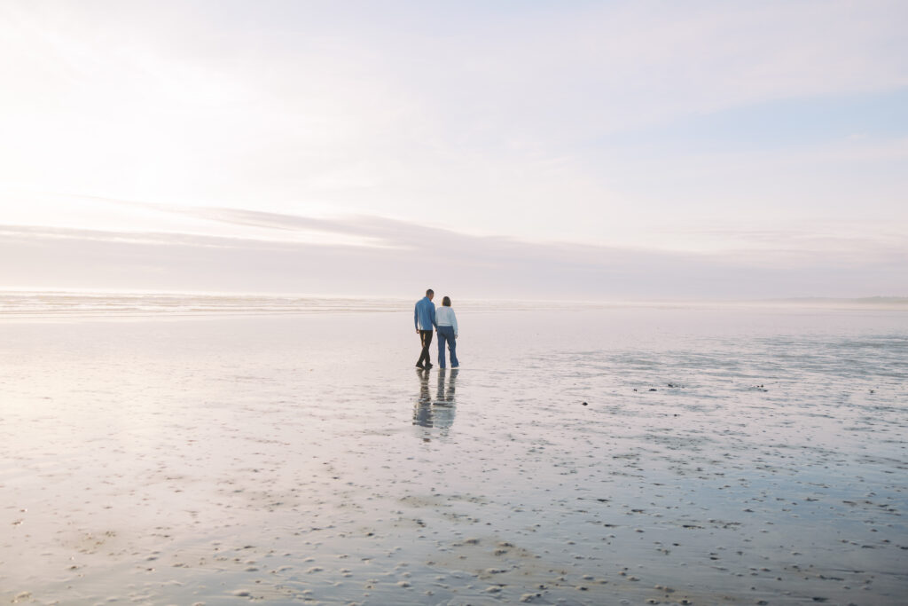 Engaged couple walking the glassy low-tide sand at Pacific Glen