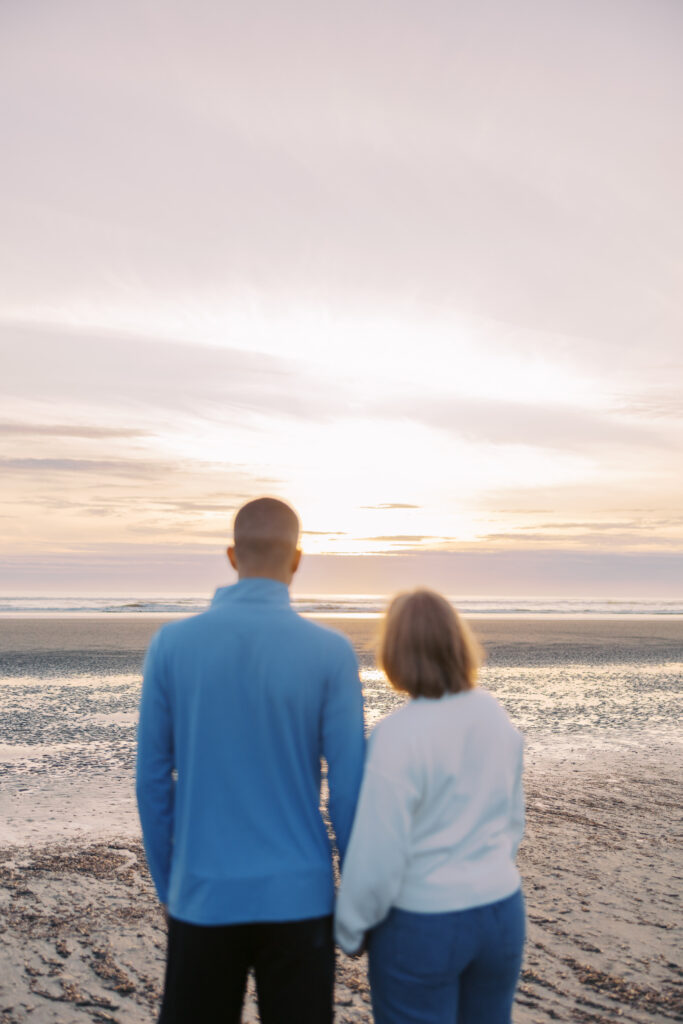 Couple holding hands and watching the sunset together at low tide
