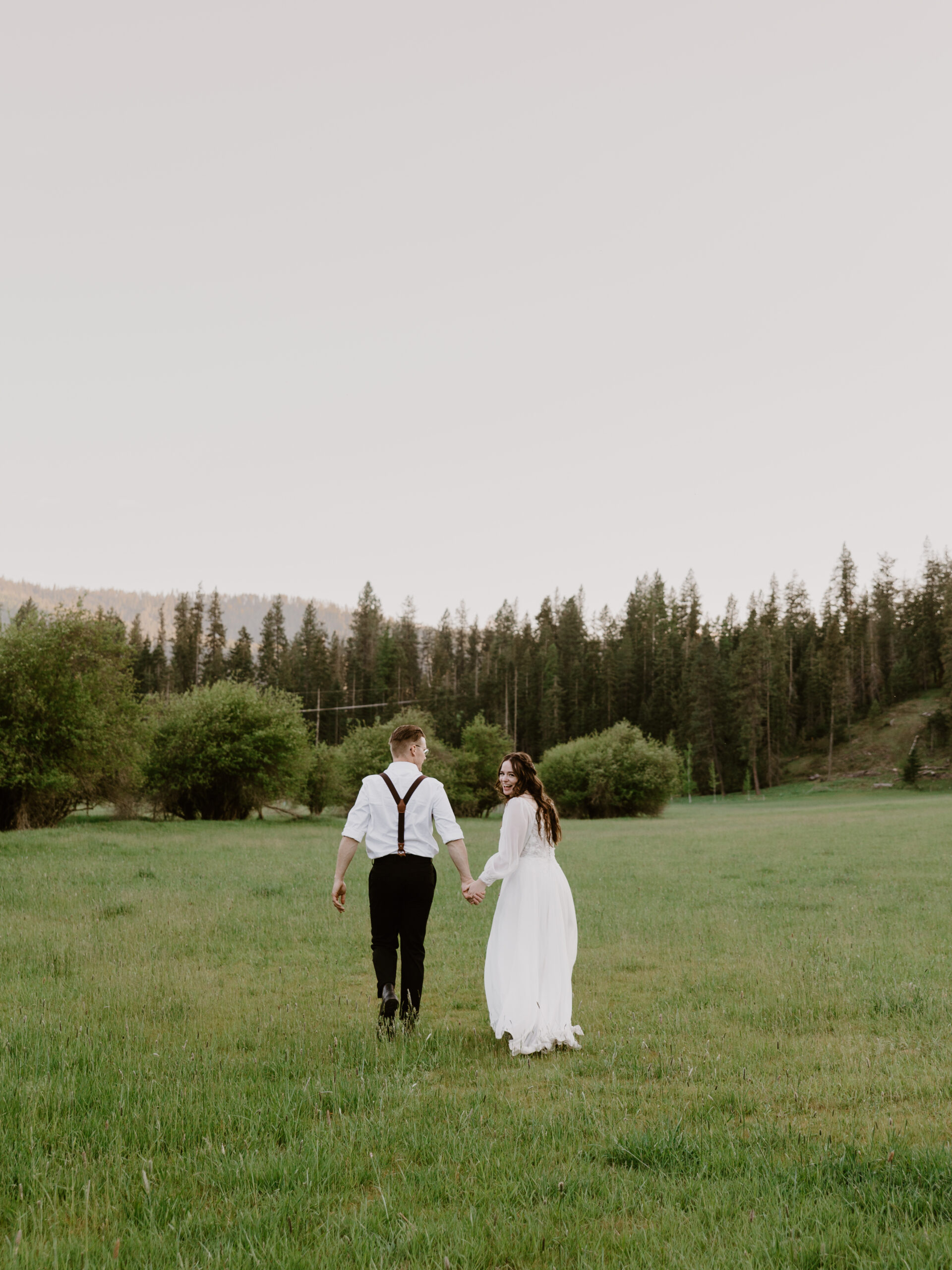 a bride and groom walking through a field in wolf lodge idaho